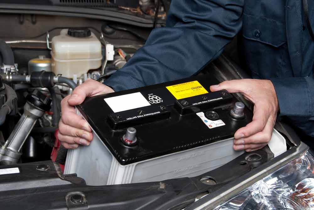 A Man Is Holding A Car Battery In His Hands — MB Automotive In Garbutt, QLD