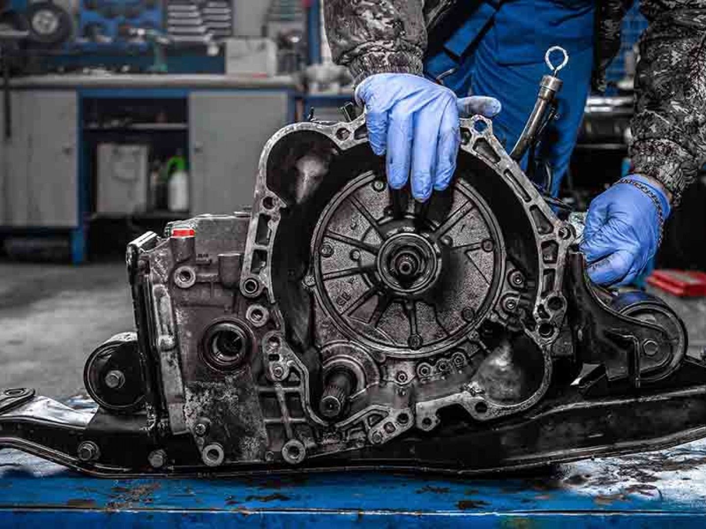 Mechanic in blue gloves working on a car transmission on a shop bench