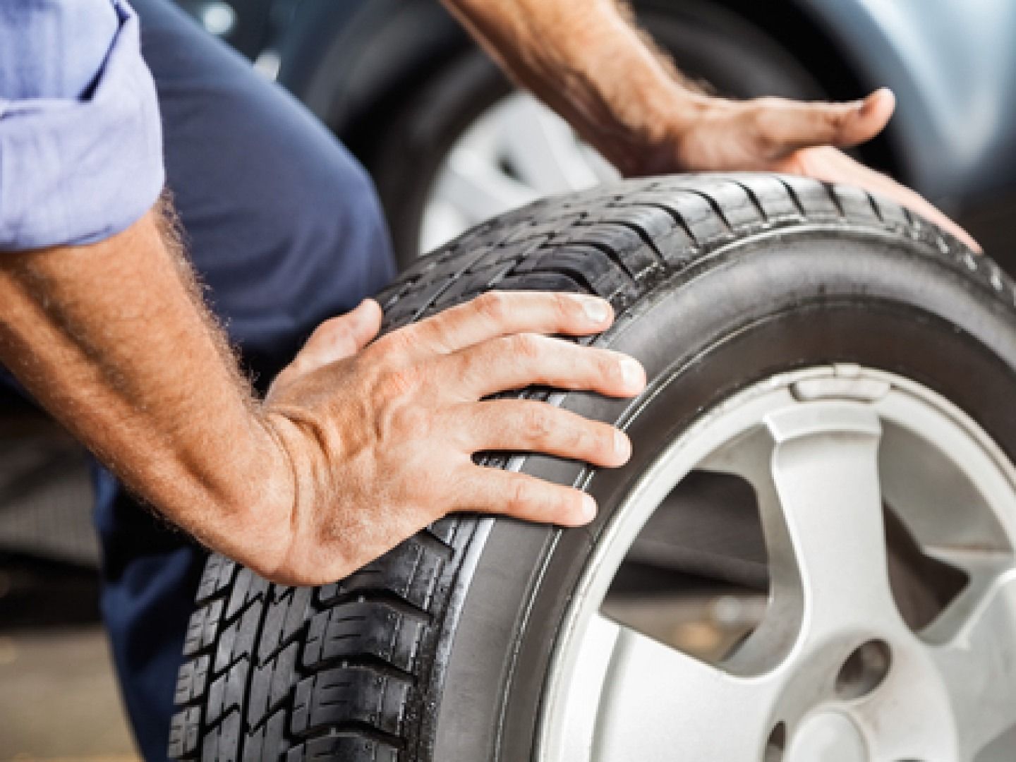 Person inspecting a car tire with hands, close-up of wheel and tread outdoors