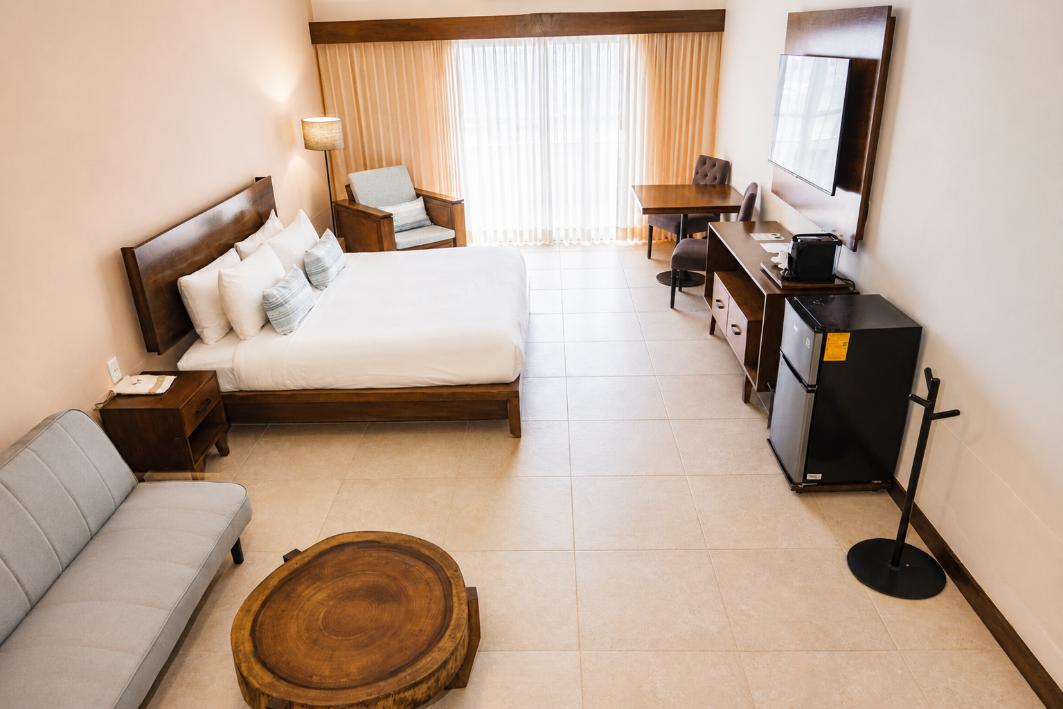 Amplio dormitorio moderno con una cama grande, una pared decorativa de madera y una luminosa zona de estar junto a la ventana.