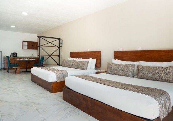 Habitación de hotel luminosa con dos camas individuales, suelo de mármol blanco y un escritorio en la parte trasera izquierda.