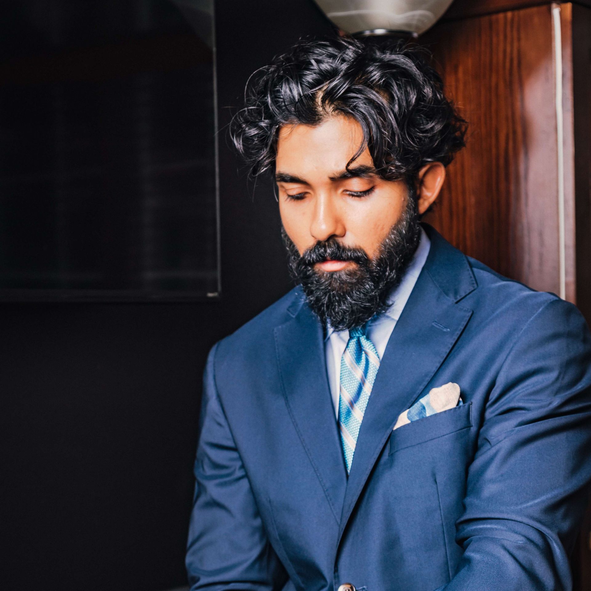 Man in a navy suit with a beard, looking down in a doorway