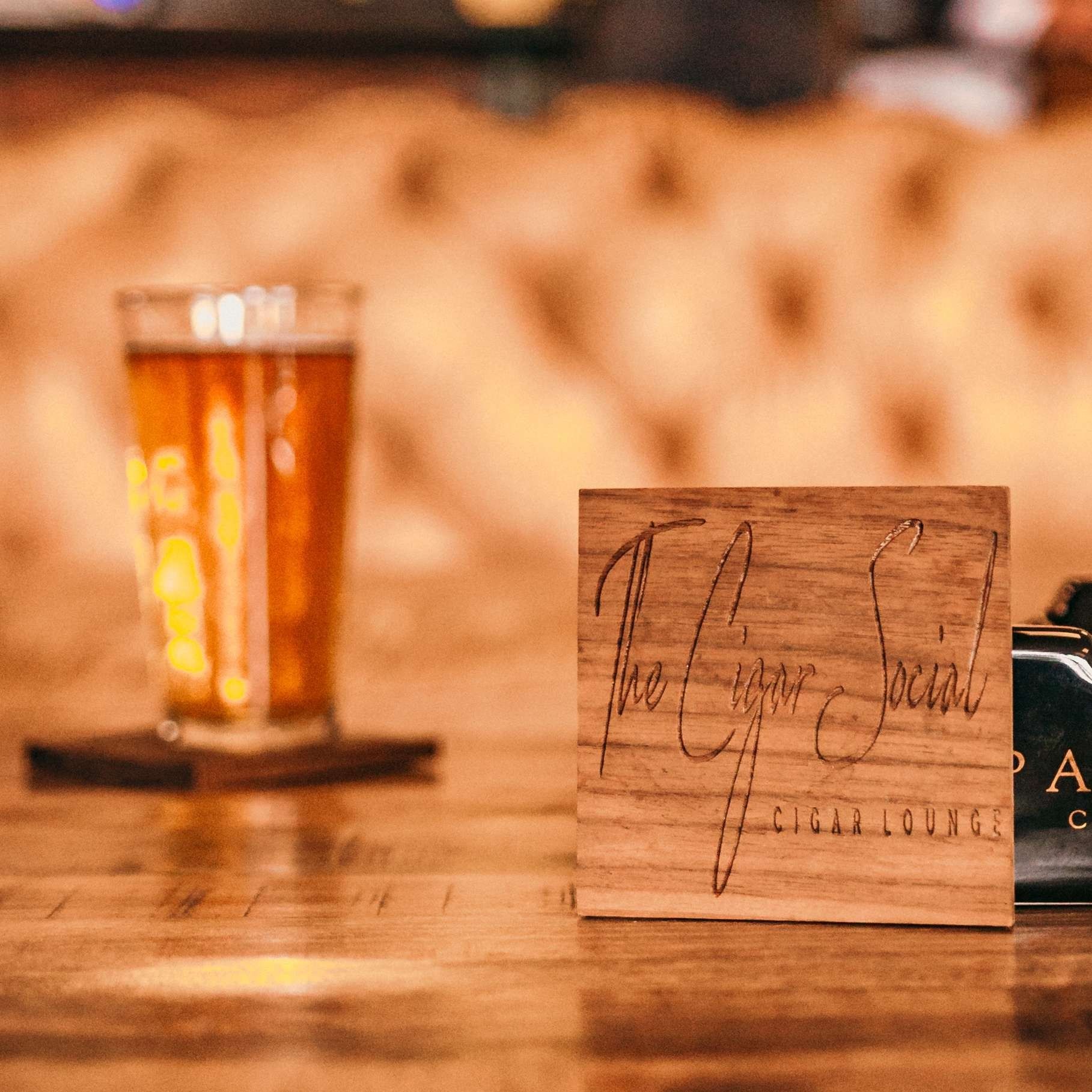 A pint of amber beer on a bar next to a small wooden sign in a warm, cozy pub