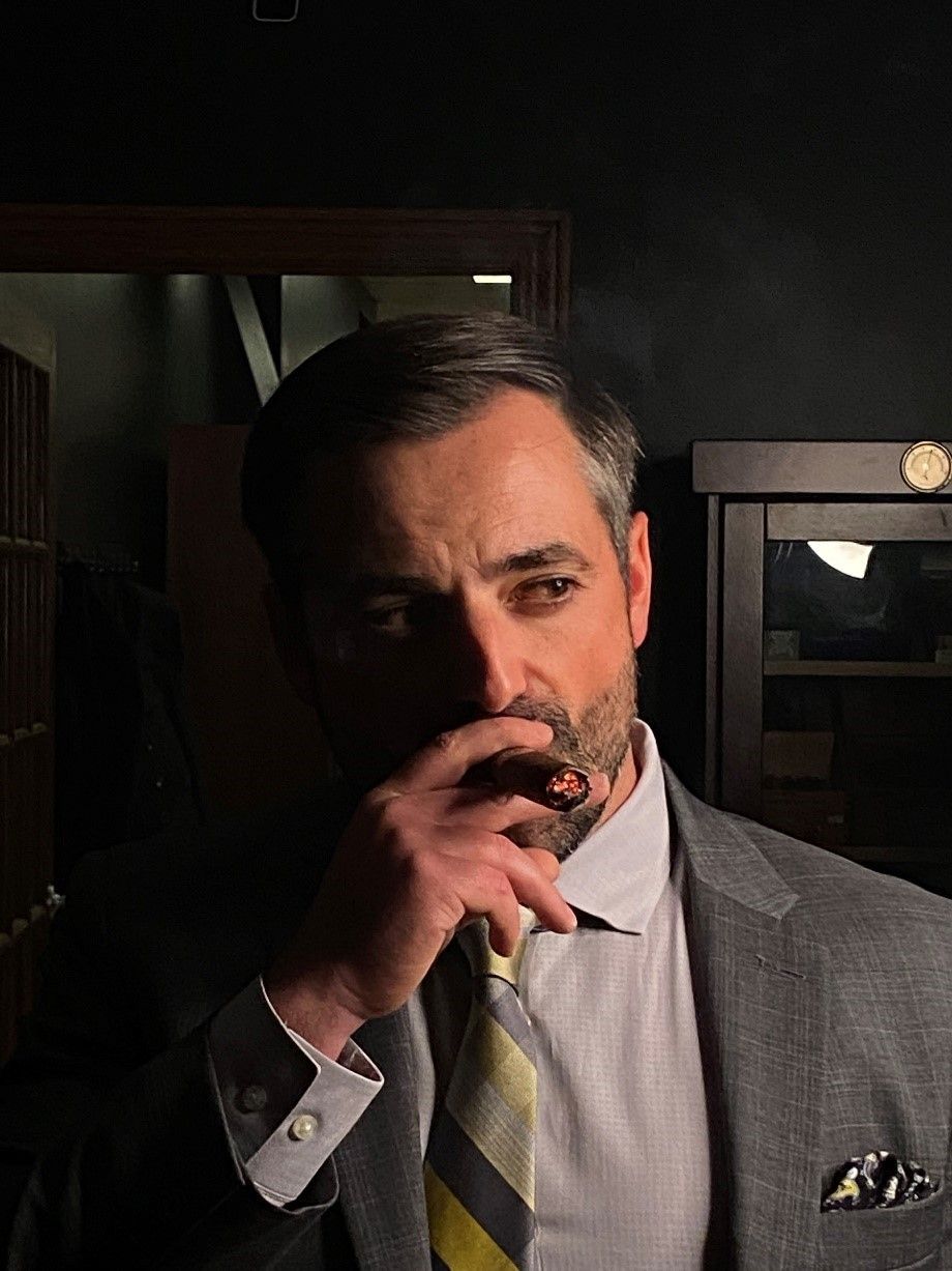 Man in a gray suit smoking a cigar in a dimly lit room
