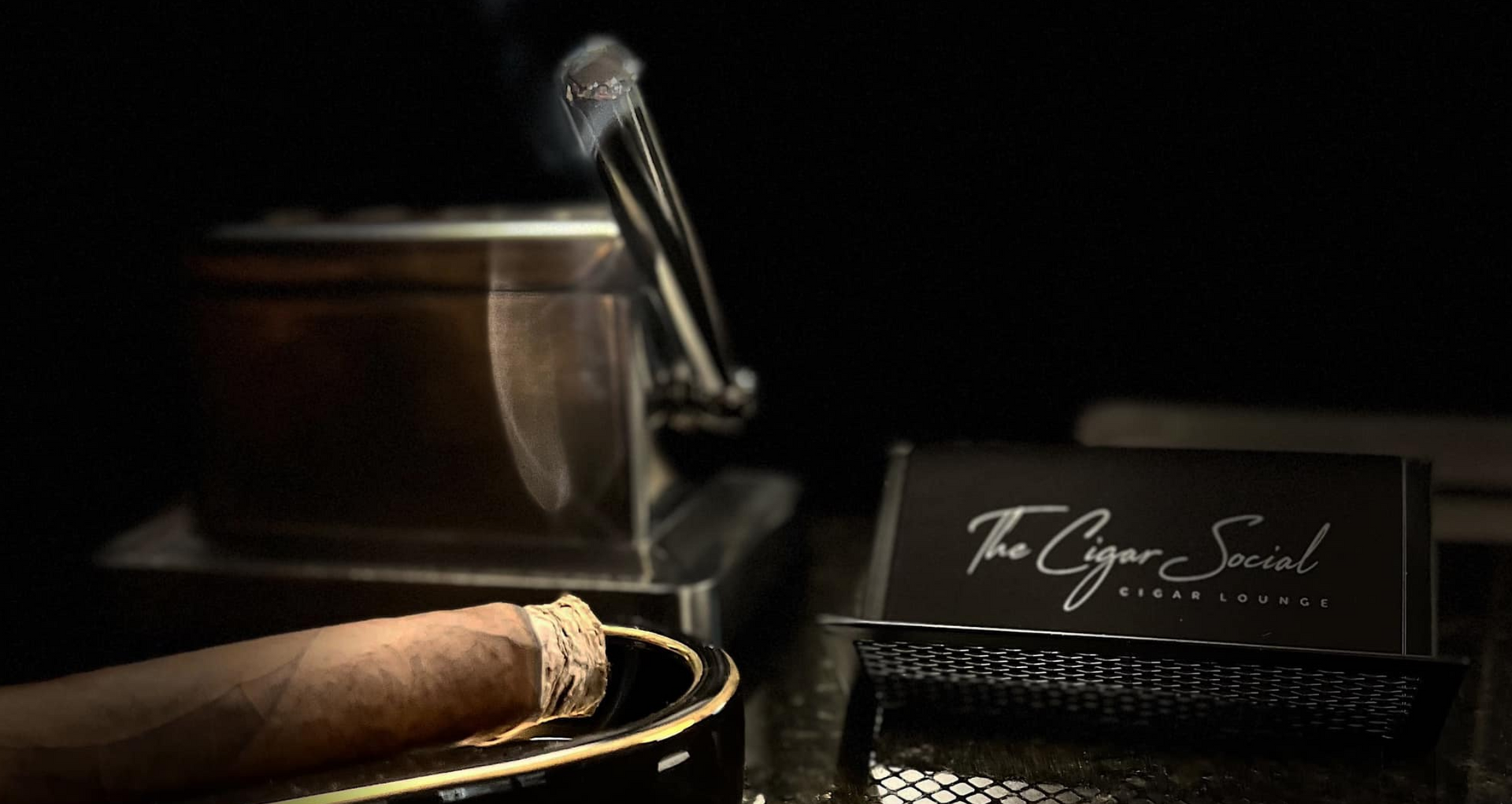 Cigar on an ashtray beside a luxury watch and business card in a dark, elegant setting
