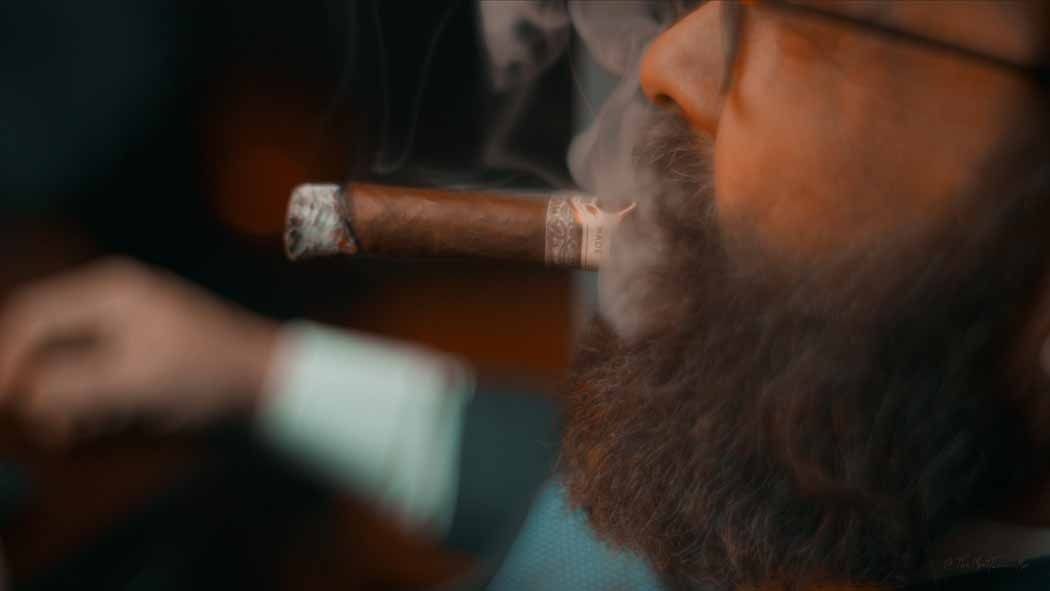 Close-up of a person smoking a cigar, with warm orange light and a blurred background