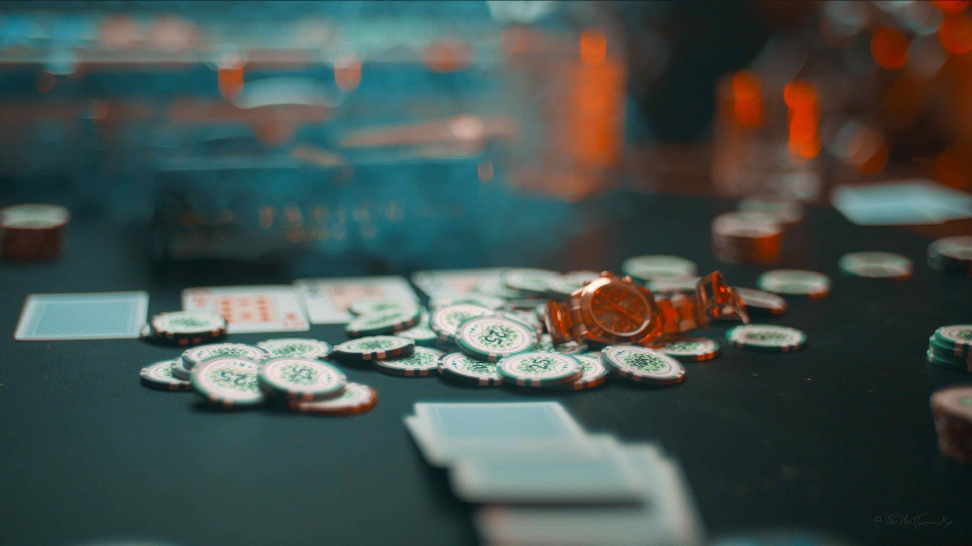 Scattered poker chips and playing cards on a casino table with warm, blurred lights in the background