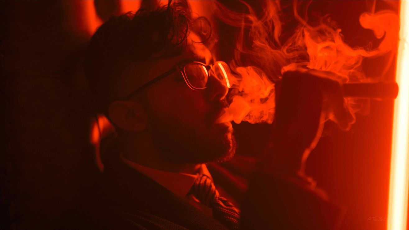 Person in glasses singing into a microphone under intense red stage lighting.