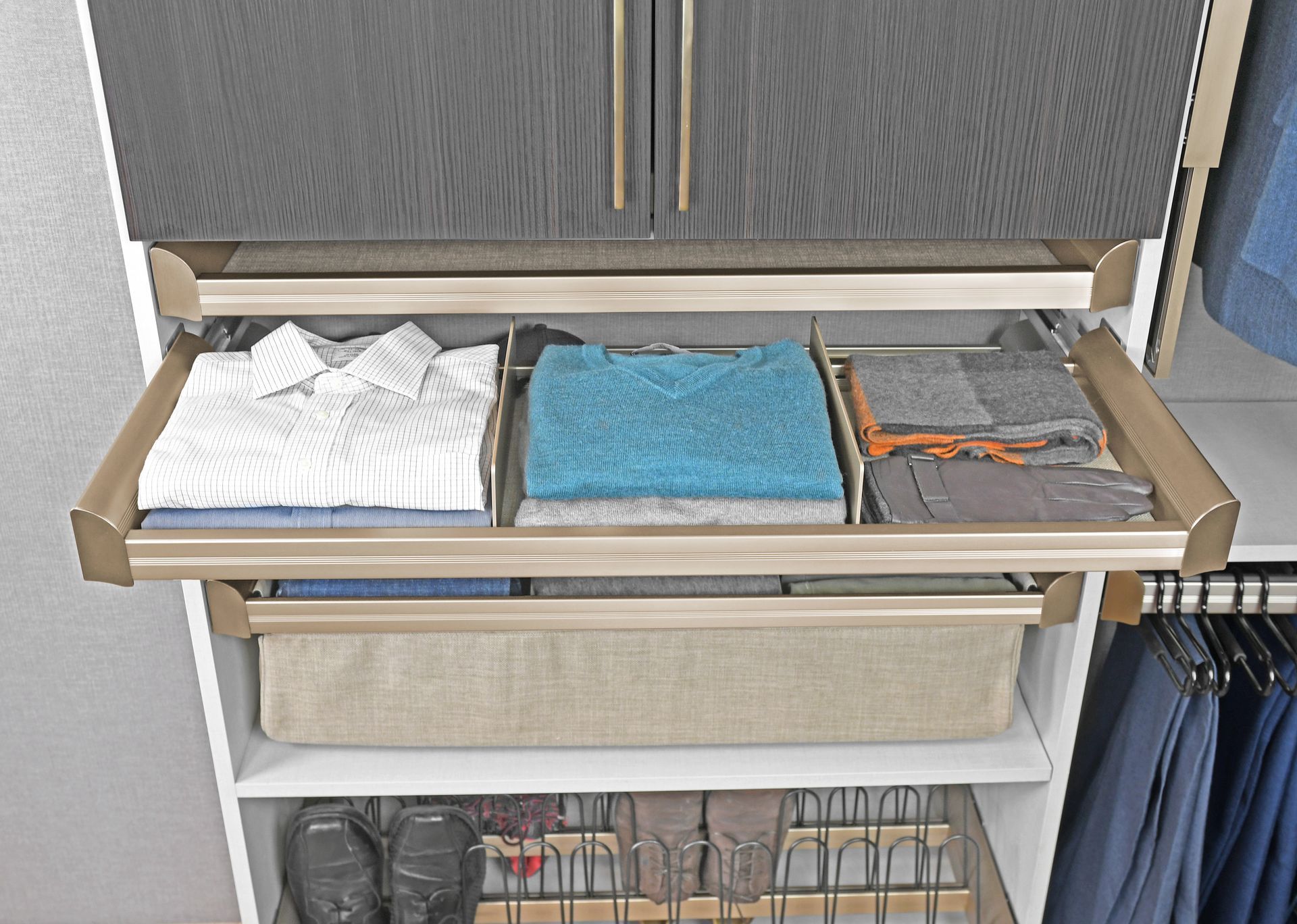 A closet organizer with pull-out shelves containing folded clothes, a storage bin, and a shoe rack at the bottom.