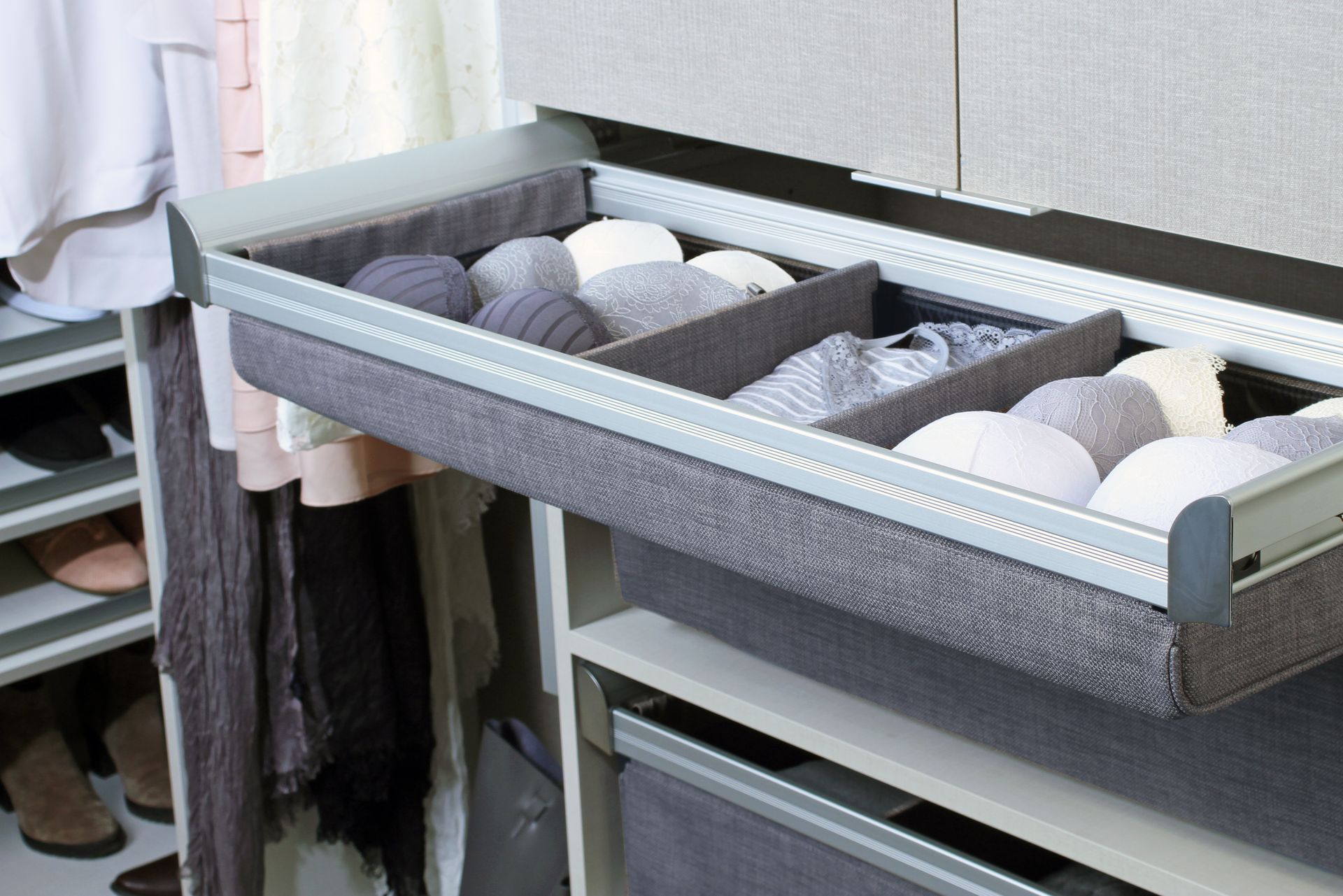 An open closet drawer featuring gray fabric dividers, organized with neatly folded items like bras and clothing accessories.