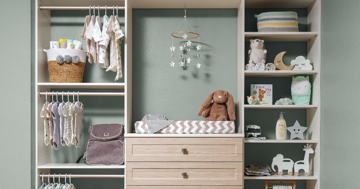 A wooden nursery closet unit with clothing racks, a changing table, shelves holding baby items, and a hanging mobile.