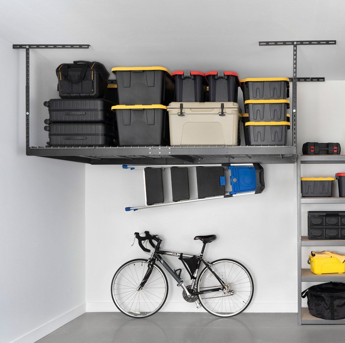 A garage features overhead storage racks holding plastic bins, a ladder mounted underneath, and a bicycle on the floor.