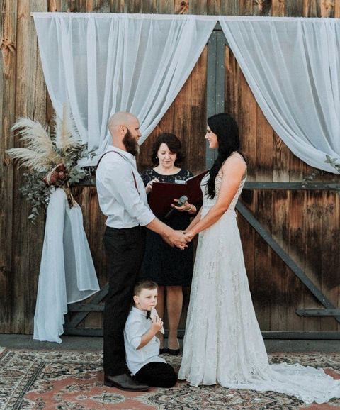 Ze and Leigh standing with their ceebrant Cheryl Warry in front of the country barn