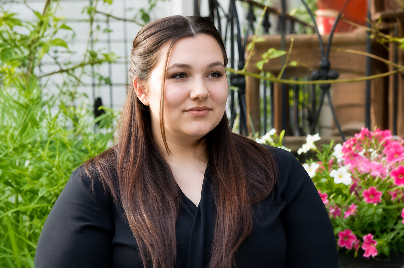 Person in a black top sitting outdoors beside pink flowers and greenery in Columbus Ohio