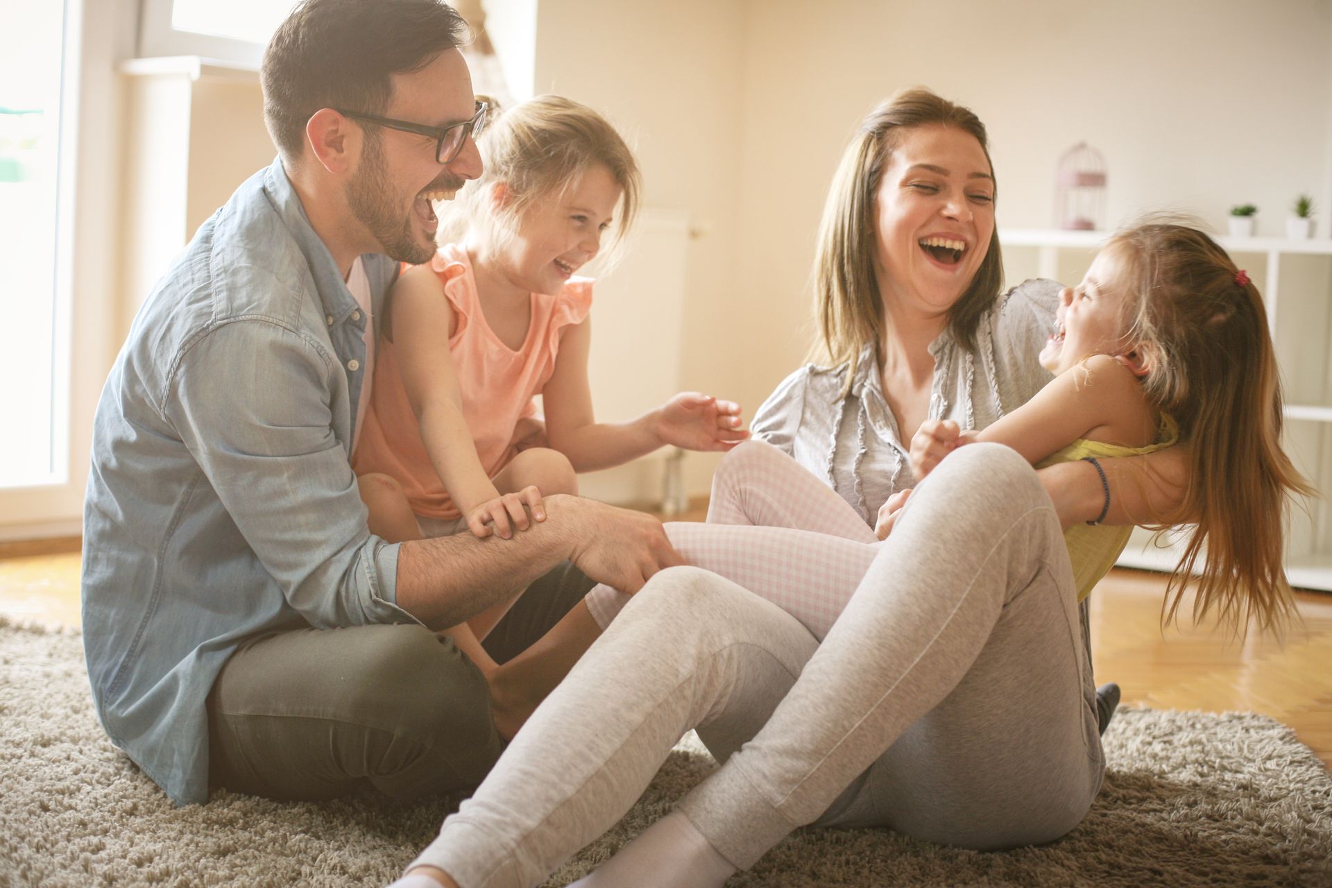 Family laughing together on a carpet in a bright living room, with two adults and two children playing.in Columbus Ohio