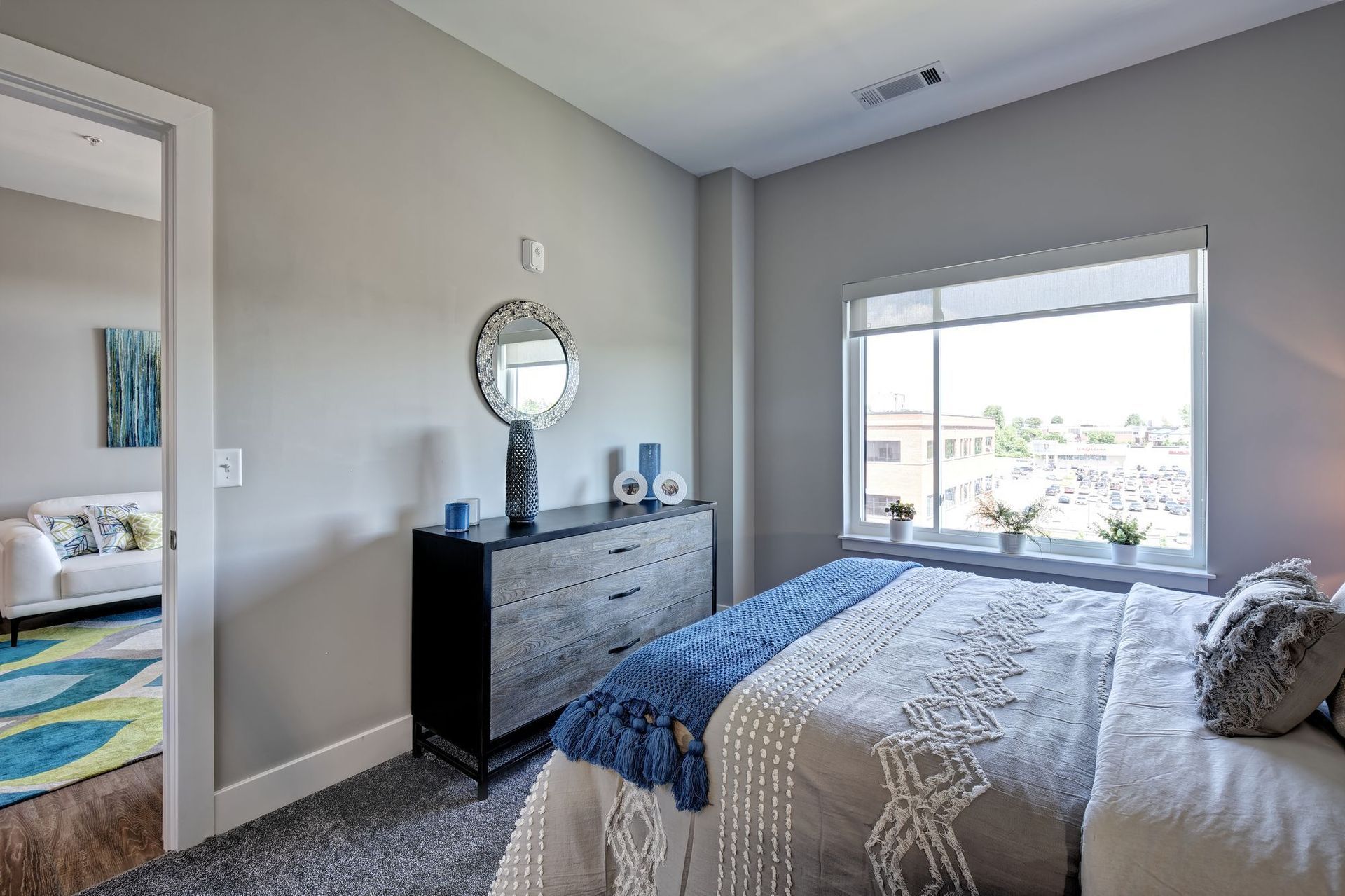 A bedroom with a bed , dresser , mirror and window.
