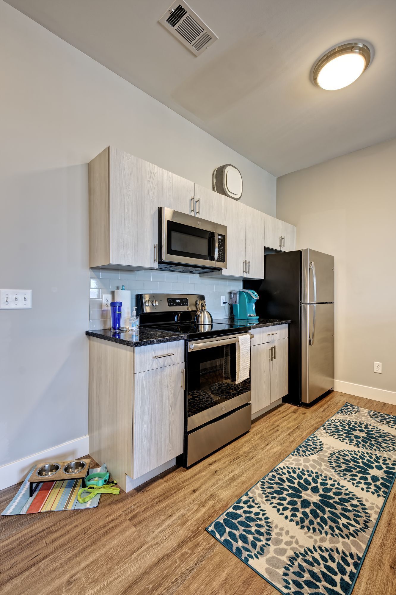A kitchen with a stove , refrigerator , microwave , and rug.