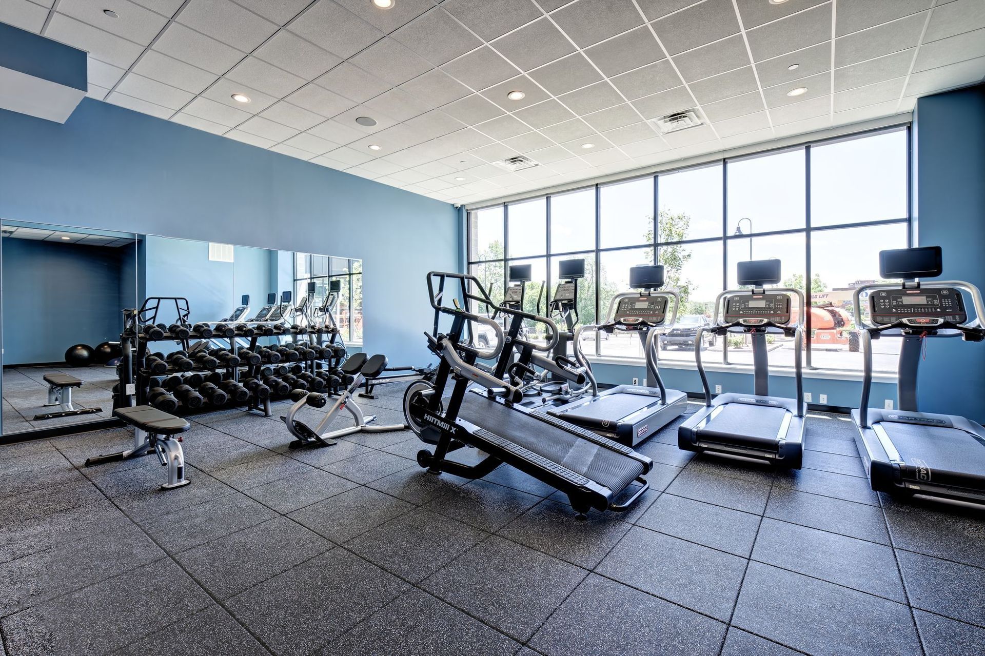 A gym with treadmills , dumbbells and a large mirror