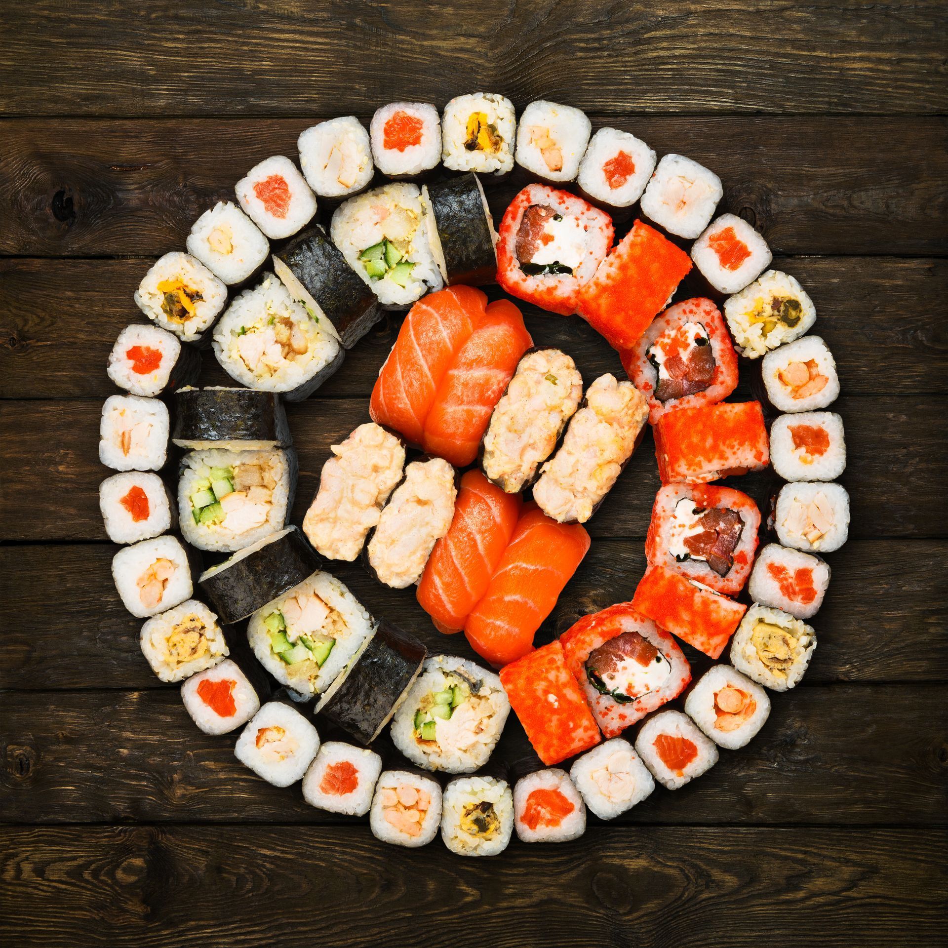 Assorted sushi rolls and nigiri arranged in concentric circles on a dark wooden table