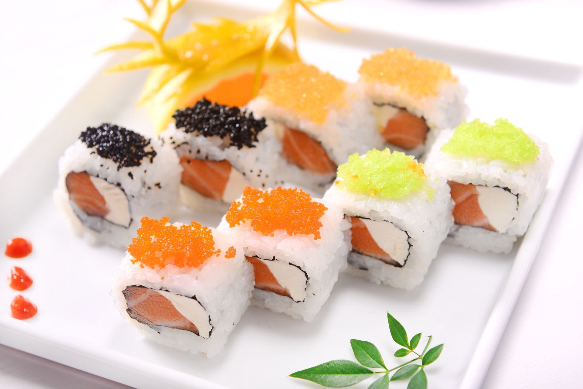 Assorted sushi rolls topped with black, orange, and green roe on a white plate with garnish