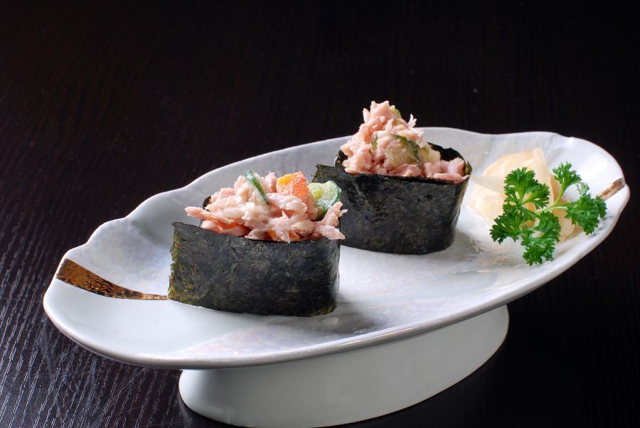 Two sushi hand rolls on a white platter, garnished with parsley on a dark background