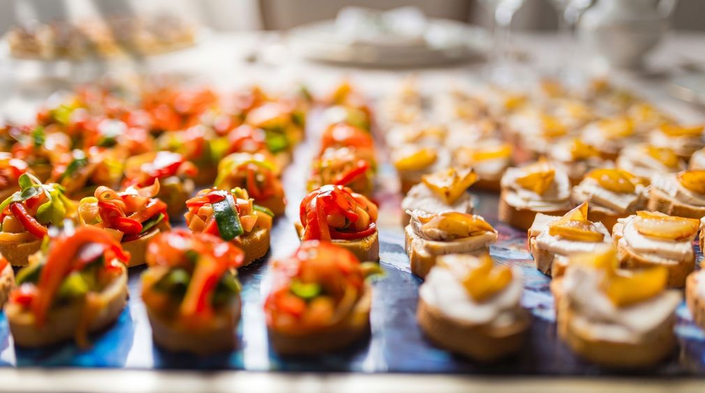Tray of assorted bite-sized appetizers with colorful toppings, arranged in rows on a serving table