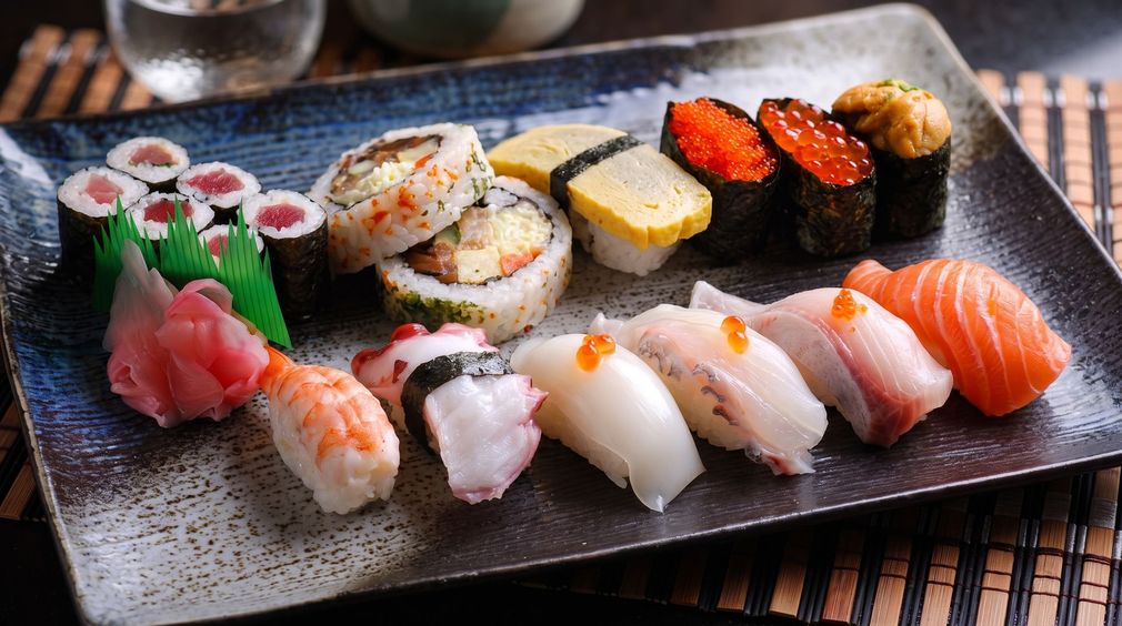Assorted sushi and sashimi arranged on a black plate with wasabi and ginger