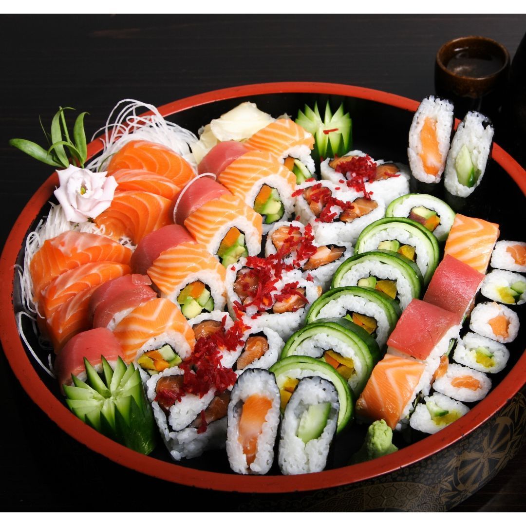 Assorted sushi rolls and sashimi arranged on a black platter with red rim.