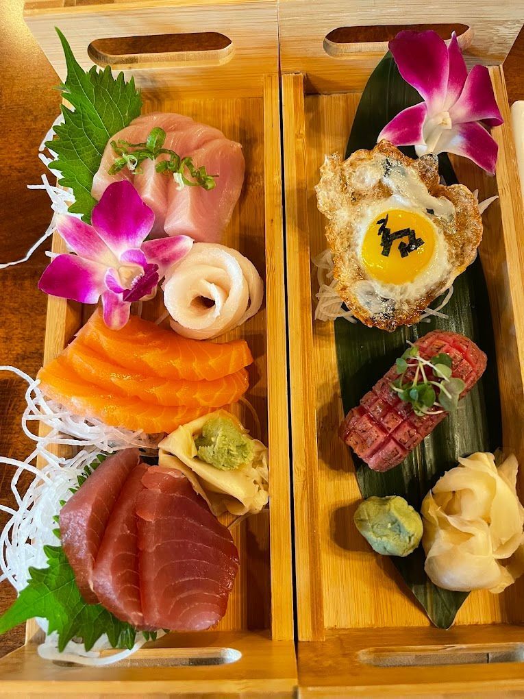 Two wooden bento boxes with assorted sushi, garnished with purple orchids and green leaves