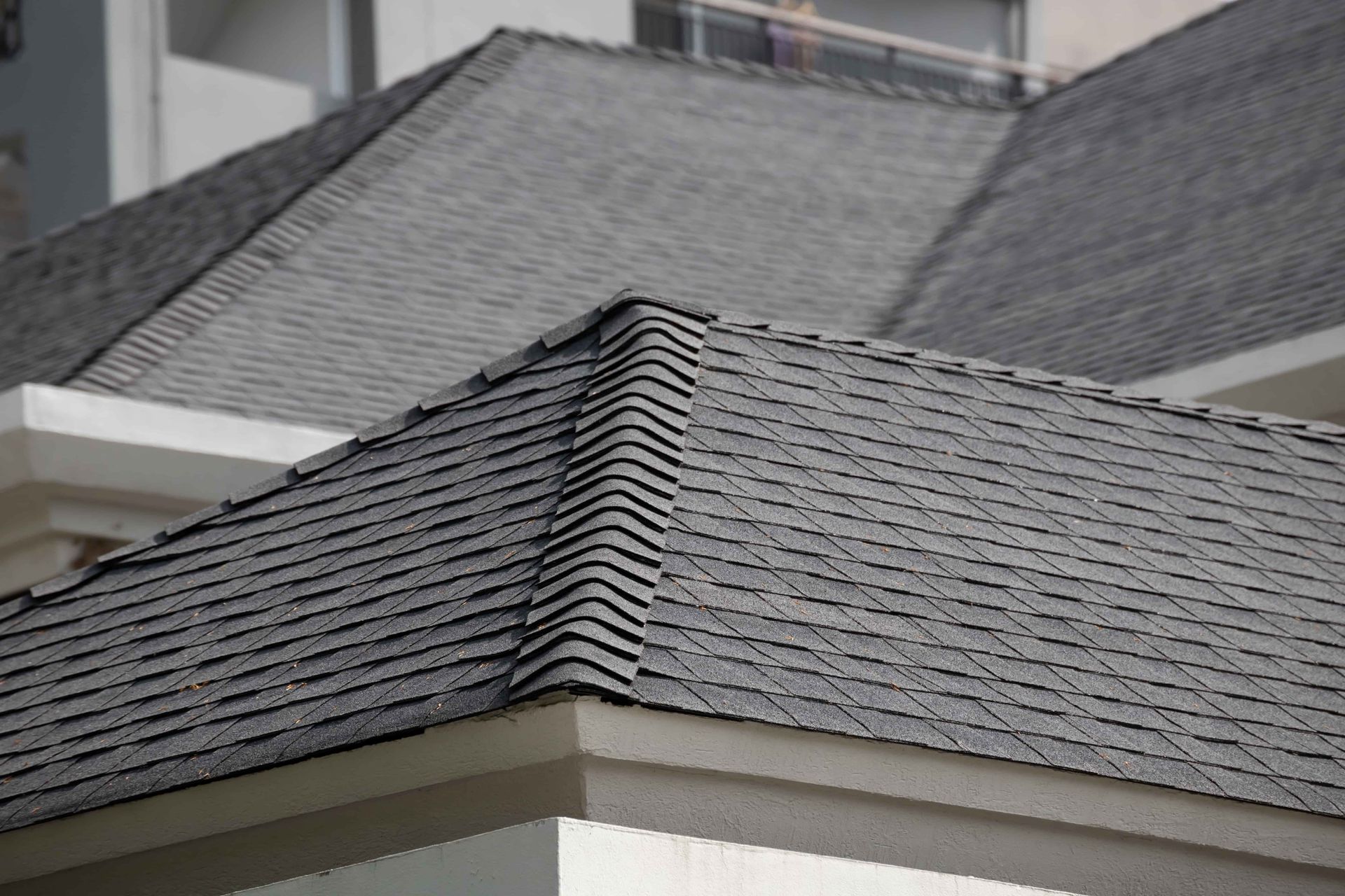Gray shingled roof corner on a house with beige trim against a blurred building background
