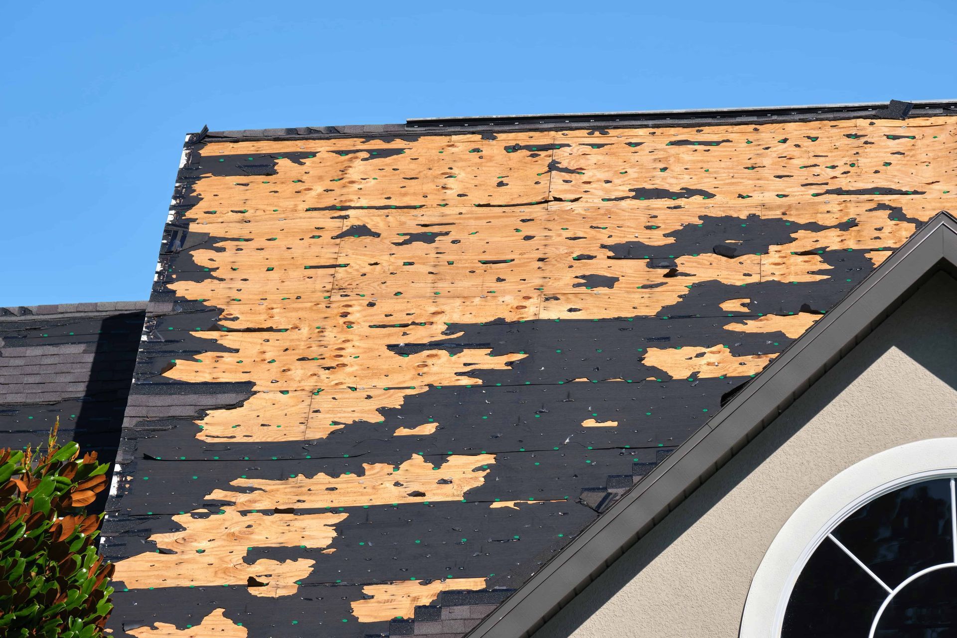 Peeling orange roof shingles exposing dark underlayment beside a dormer window
