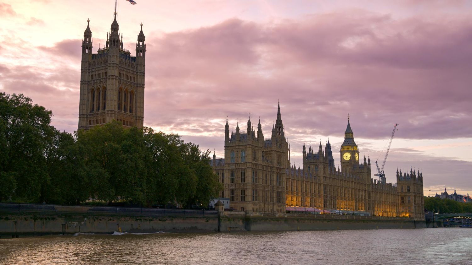 The Houses of Parliament in London at dusk, with the illuminated Elizabeth Tower reflected in the River Thames.