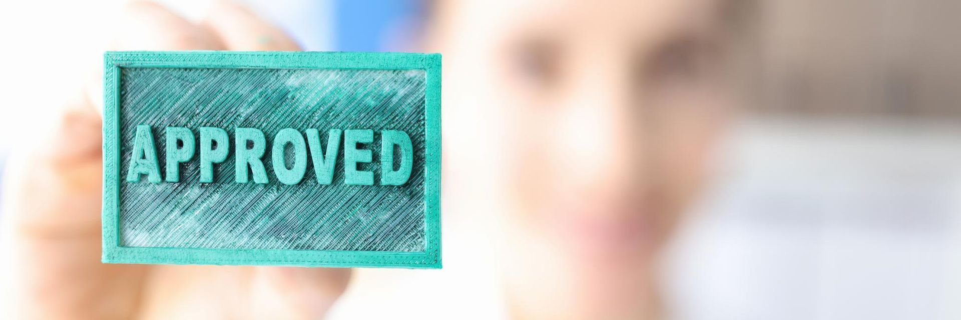 A hand holds a rectangular teal sign with the word