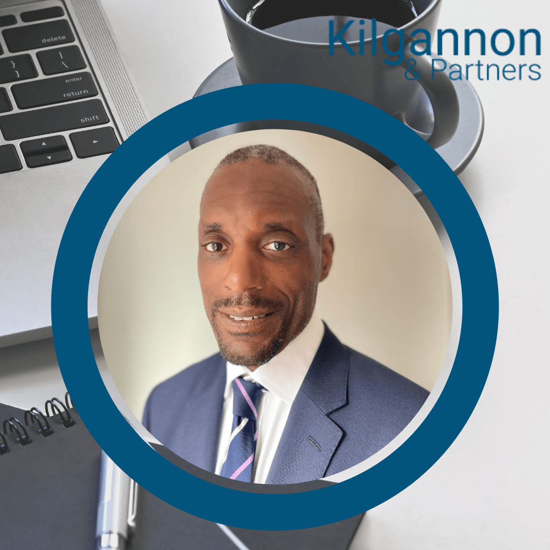 Headshot of a man in a blue suit and striped tie, framed in a circle against an office background with a laptop and coffee.