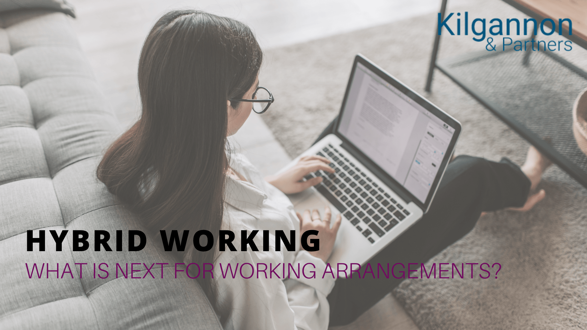 A person works on a laptop while sitting on the floor by a sofa. Text overlay: 