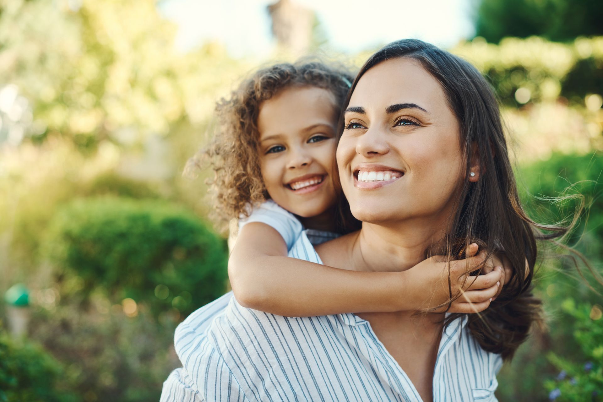 Woman smiles while a child hugs her, outside.
