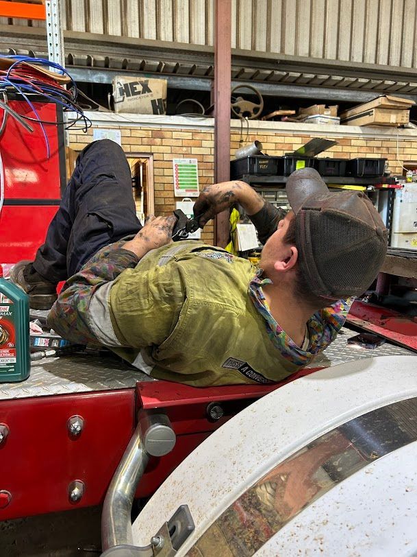 A Man is Laying on the Back of a Truck in a Garage — Trucks On The Run Pty Ltd in Westbrook, QLD