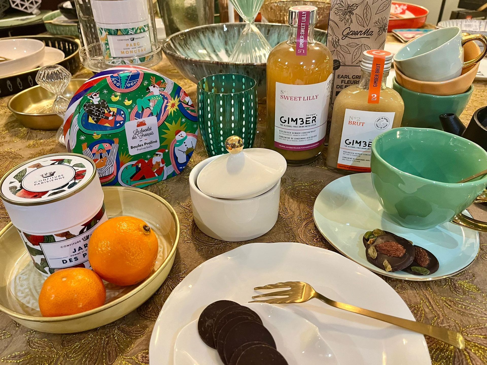 Une table surmontée d'assiettes, de bols, de tasses, de bouteilles et d'oranges.