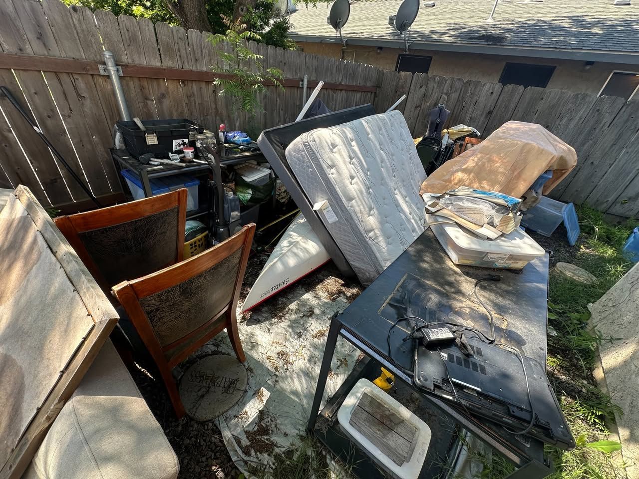 Hoarder Cleanout in Butte County, CA — before: cluttered backyard with pile of old furniture and boards
