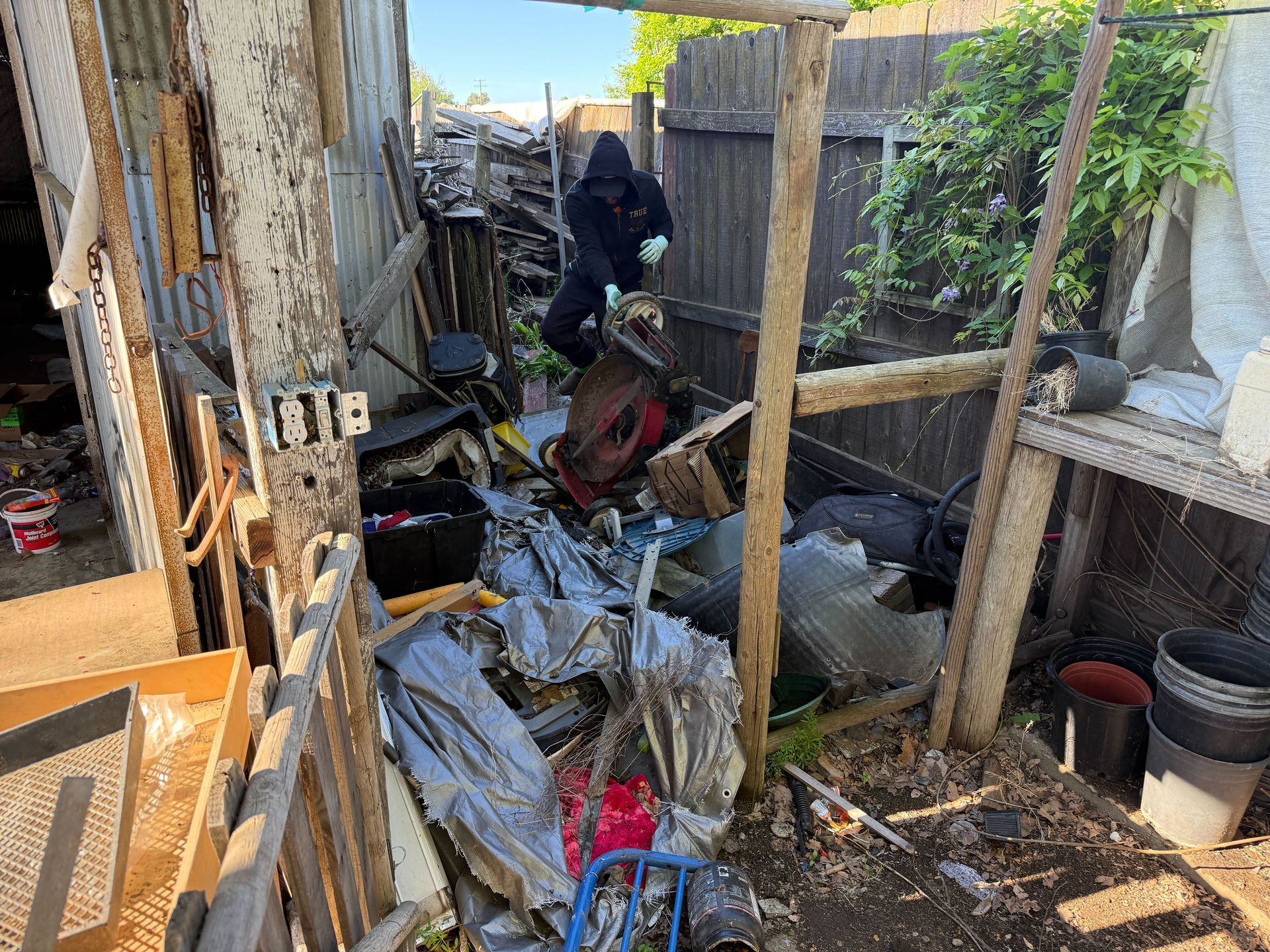 Hoarder cleanout in Gridley, CA — before: fenced outdoor area filled with junk and debris