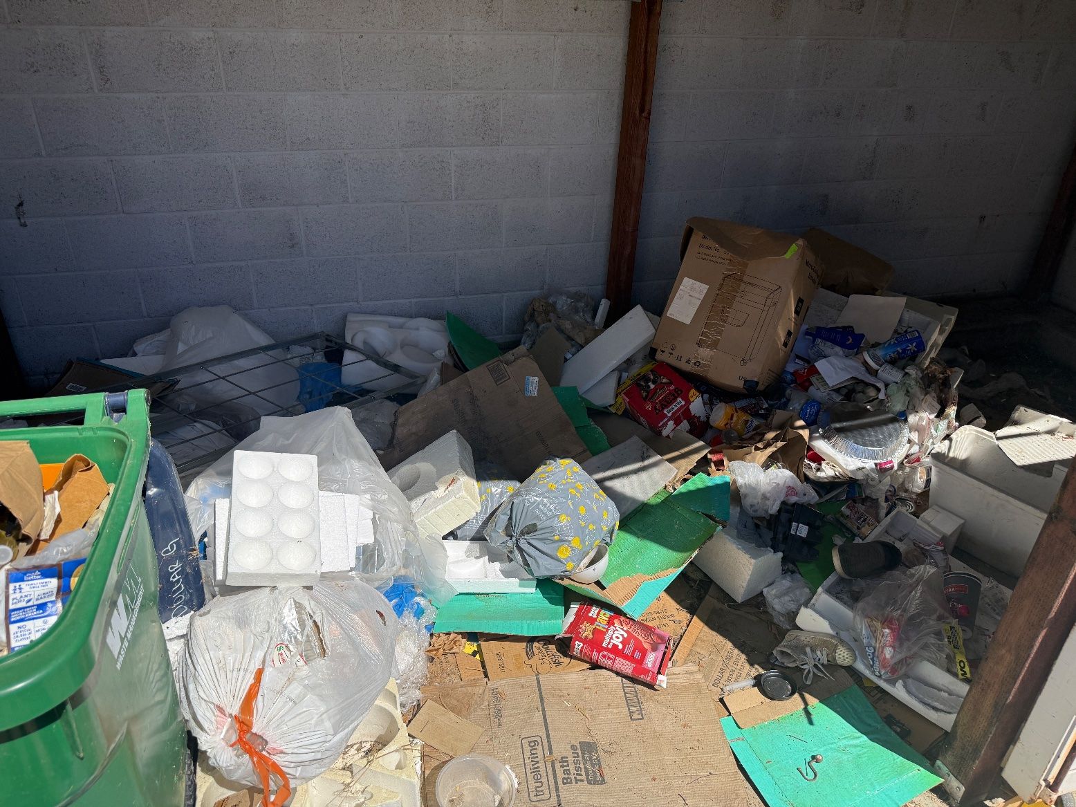 Junk piled in a commercial dumpster enclosure before cleanup.