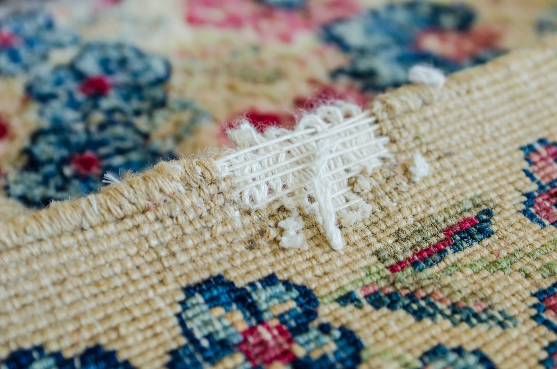 Close-up of a beige floral rug with a white snagged thread on the woven surface Close-up of a beige floral rug with a white snagged thread on the woven surface
