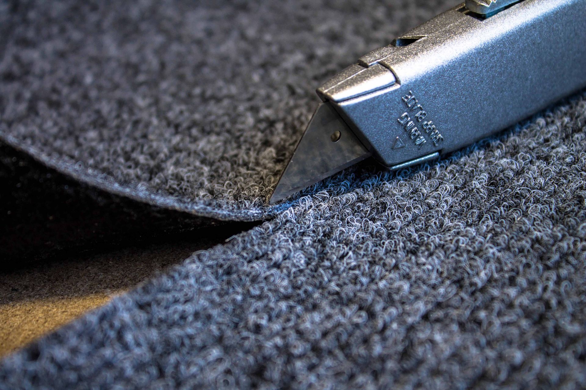 Close-up of a utility knife cutting dark textured fabric on a work surface Close-up of a utility knife cutting dark textured fabric on a work surface