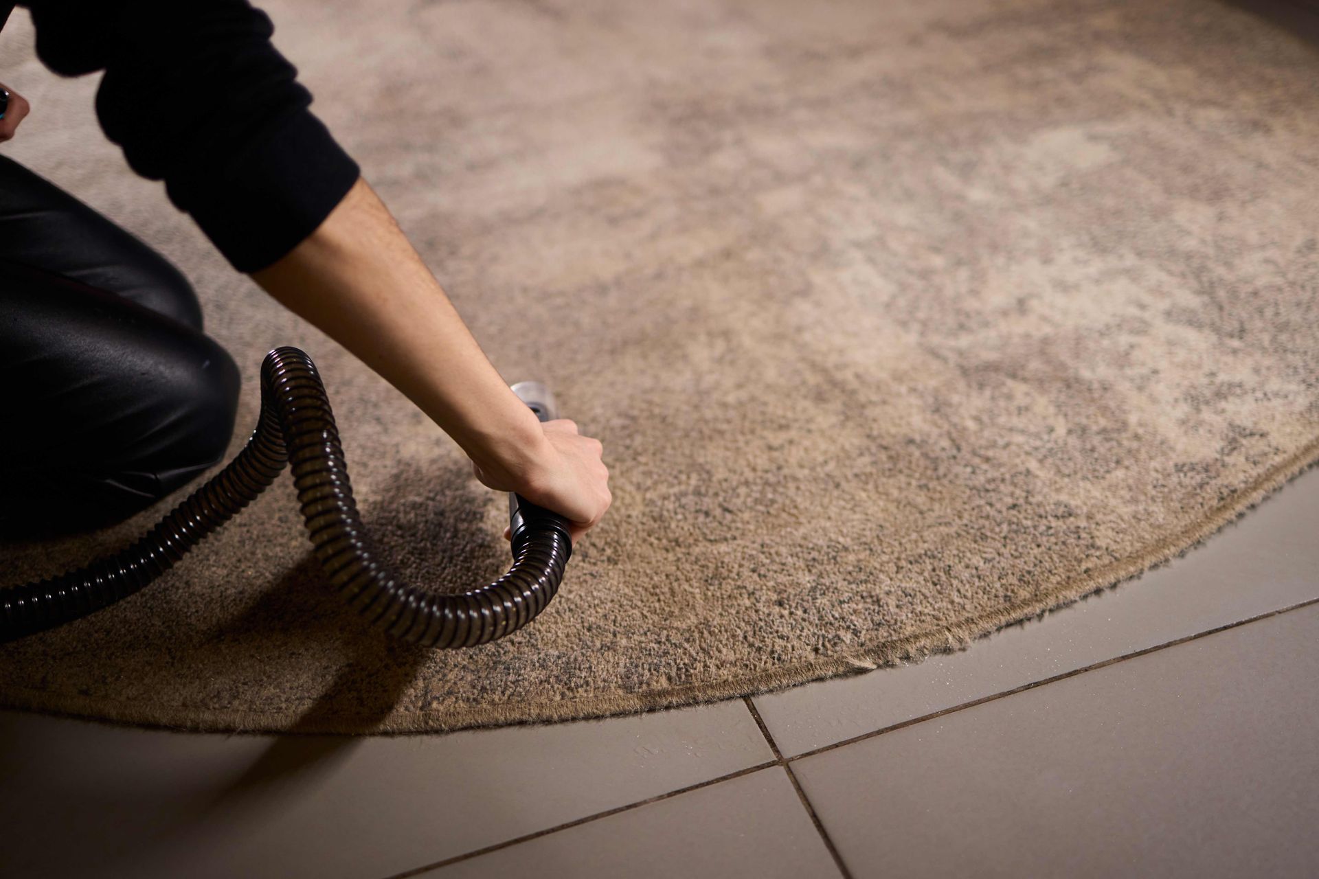 Person vacuuming a beige carpet beside tile flooring Person vacuuming a beige carpet beside tile flooring