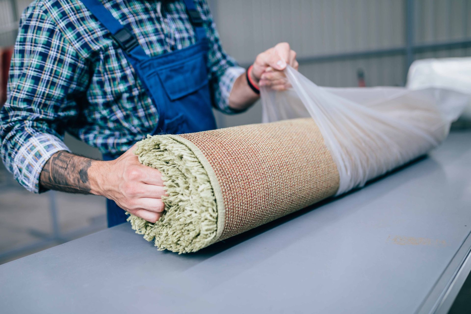 Worker rolling a large beige carpet onto a table in a workshop Worker rolling a large beige carpet onto a table in a workshop