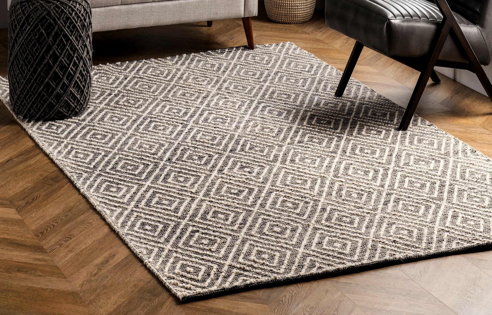 Patterned beige area rug on a hardwood floor beside a chair and table in a living room Patterned beige area rug on a hardwood floor beside a chair and table in a living room