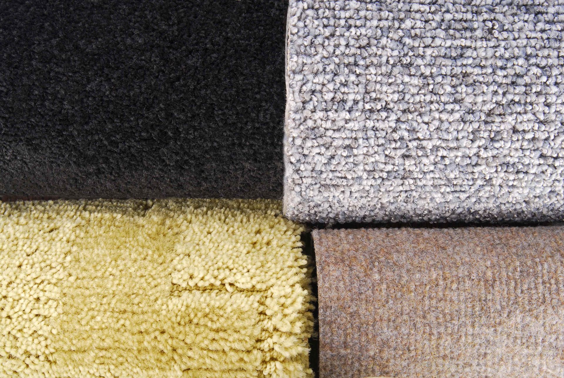 Close-up of four textured carpet samples in black, gray, yellow, and beige. Close-up of four textured carpet samples in black, gray, yellow, and beige.