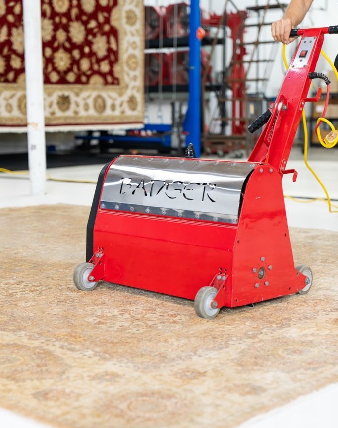 Patterned rug being washed on industrial rollers, with water flowing over the red and gold fabric