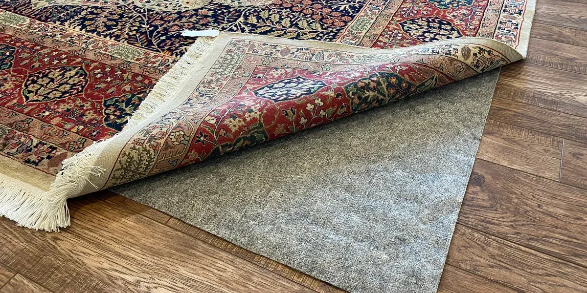 Person rolling up a large beige carpet in a room with speckled flooring. Person rolling up a large beige carpet in a room with speckled flooring.