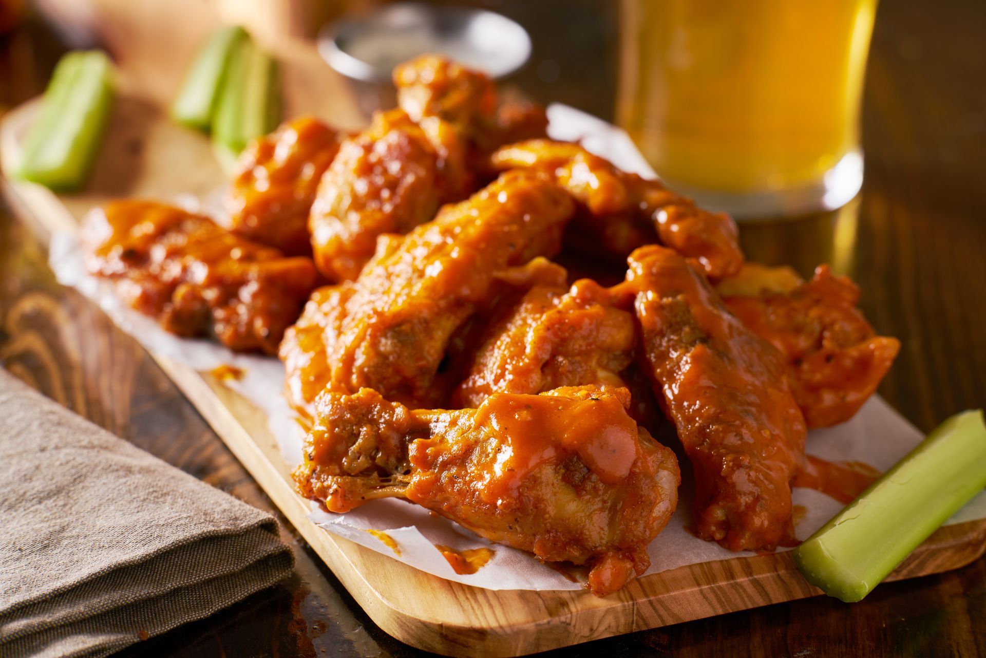 Buffalo wings on a wooden serving board with celery sticks and a glass of beer